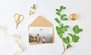 Hochzeitskarte als Einladung, romantisches Paar auf Einladungskarte, rustikaler Umschlag, goldene Klammern im Hintergrund