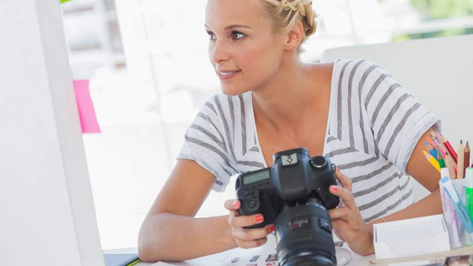 Blonde Frau im gestreiften Shirt hält eine Kamera; Erklärung verschiedener Formate: JPEG (auch JPG) Images und RAW Files