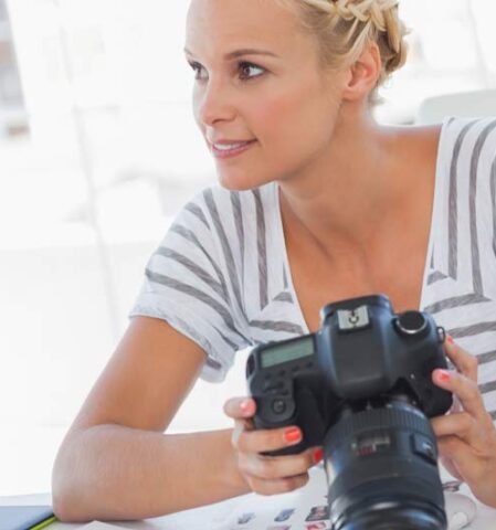 Frau mit Fotoapparat vor einem Bildschirm