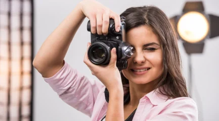 Eine Fotografin hält sich eine Kamera vors Gesicht und macht ein Bild, wahrscheinlich ein Portraits